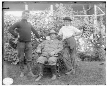 Three men posed in residential garden; the man seated is Ben Pearson