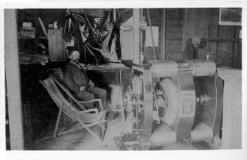 Man dressed in clothing from the early 1900s siting by electrical equipment