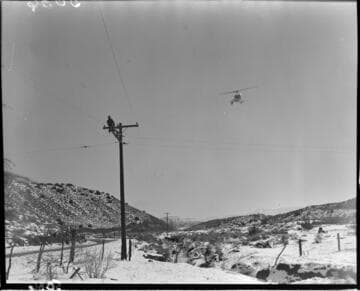 Linemen working at the top of a pole in the snow with helicopter flying near by