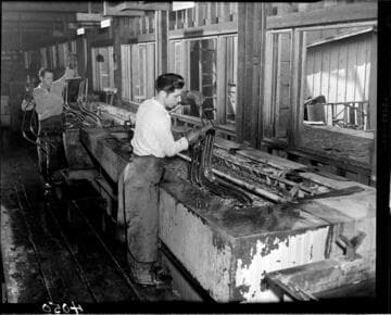 Men electroplating metal parts in a long tank with liquid