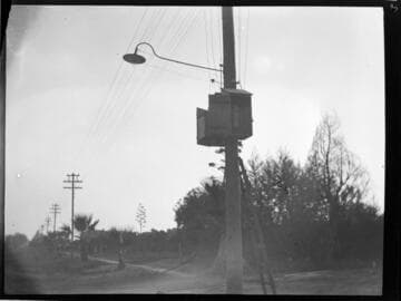 Double circuit wood pole distribution line with communications box (?) and light on nearest pole
