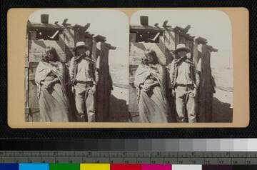 A native man and woman, most likely Hualapai, stand in front of a wooden shelter