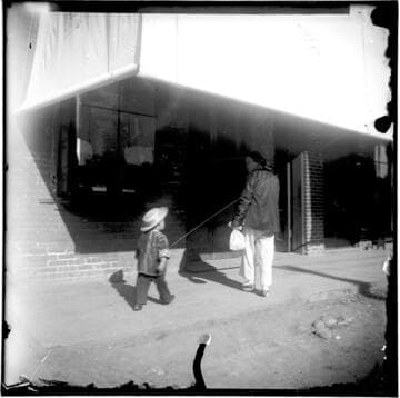 Adult and child walking on street, near building