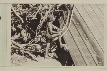 Norm Nevills posed at wreck of the Bur. of Reclamation pontoon which was lost at Lees Ferry, lodged on top of the rock at Bedrock Rapid in 1947, and landed on the left bank near Mile 193