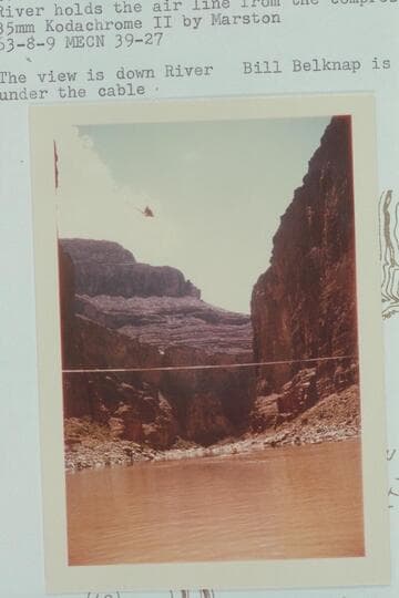 Lynn Roberts in his helicopter working as the elevator at the Marble Canyon Dam site.  The cable across the river holds the air line from the compressors at the rim.  The view is downriver.  Bill Belknap is in his Sportyak under the cable