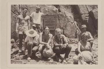Part of  Nevills party posed in front of plaque at Separation Canyon.Garth Marston at left;Norm Nevills with hand on plaque.Marie Saalfrank ducks her head.Anne and Zoe Desloge crouch at front center.Kent Frost and Margaret Marston at right