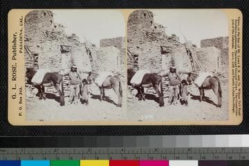 A Hopi man, child and two mules standing in an unidentified pueblo