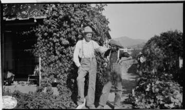 An older man and a boy standing in front of a residence covered by ivy