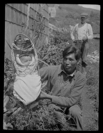 An unidentified Native American man holding baby in a cradle- board