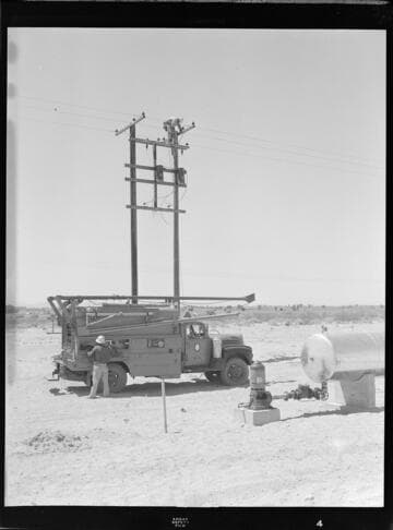Linemen installing transformers on a pair of distribution poles in the desert