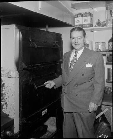 Man in suit standing next to commercial  electric oven in restaurant kitchen