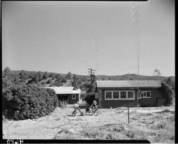 Two children on bicycles in backyard with dog