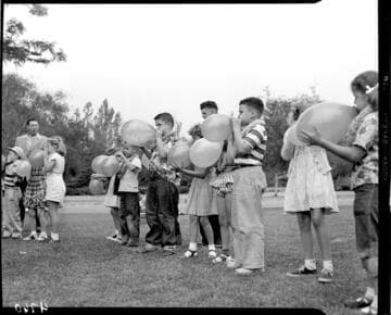 Kids in the park blowing up balloons