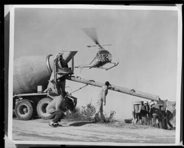 Helicopter flying hods of wet concrete into remote tower construction sites